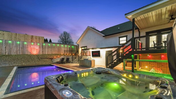 A hot tub and swimming pool in a backyard with a wooden fence and a house in the background.