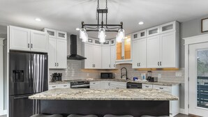 A modern kitchen with white cabinets, a stainless steel refrigerator, a granite countertop, and a central island with bar stools.