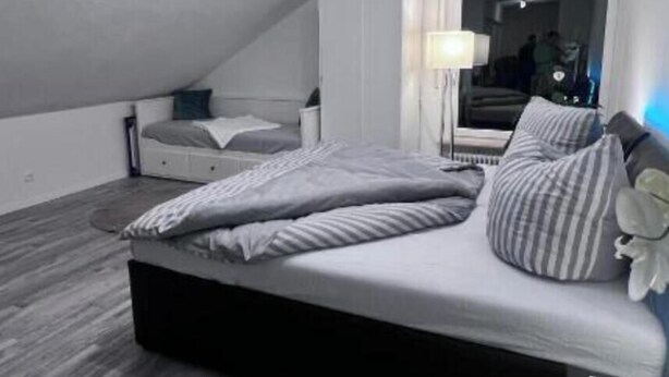 Ein Schlafzimmer mit einem Bett, einem Nachttisch, einer Lampe und einem Fenster.