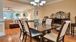 Uma sala de jantar com uma grande mesa de madeira, cadeiras estofadas e um candelabro.