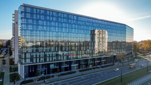 En modern byggnad med glasfasad som reflekterar omgivningen, troligen ett hotell, med skyltar på ett främmande språk.