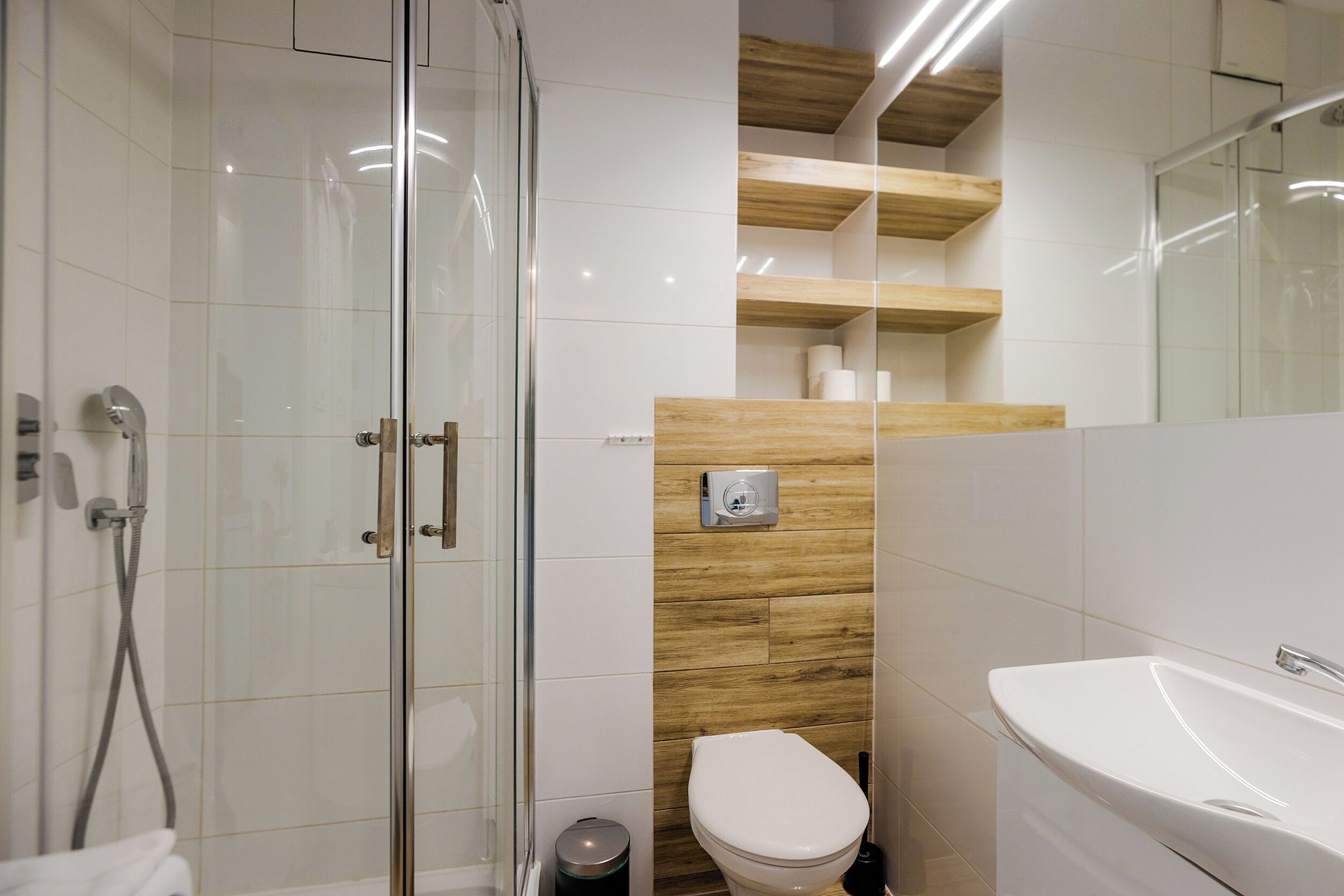 Een moderne badkamer met een douchecabine van glas, een wit toilet en een witte wastafel.