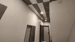 Un pasillo estrecho con techo a la vista y vigas expuestas, además de una lámpara. Se observan dos puertas, una con manija de metal y la otra con manija negra.