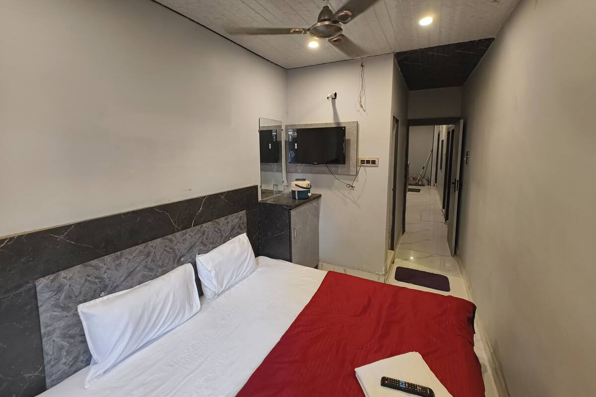 A hotel room with a bed, a ceiling fan, a TV mounted on the wall, and a hallway leading to other rooms.