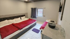 Un dormitorio con cama, ventana con cortinas, ventilador de techo y una mesita con una tetera.