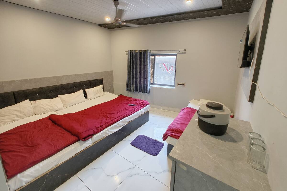 A bedroom with a bed, a window with curtains, a ceiling fan, and a small table with a kettle.