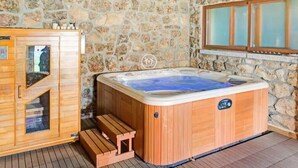 Une pièce aux murs de pierre, dotée d’un sauna en bois, d’un jacuzzi et d’un meuble en bois avec une porte en verre.