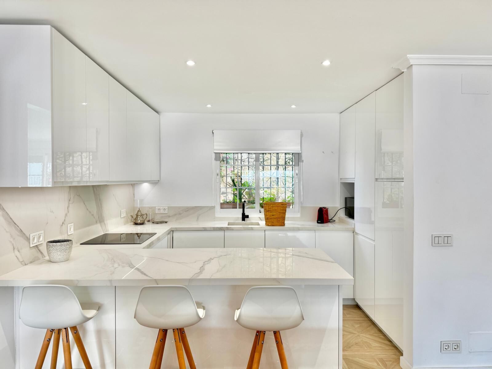 Une cuisine moderne avec des meubles blancs, un plan de travail en marbre et un îlot central doté de tabourets de bar.