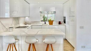 A modern kitchen with white cabinets, a marble countertop, and a central island with bar stools.