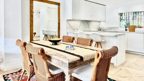 A modern kitchen with white cabinets, a marble countertop, and a dining area with wicker chairs and a wooden table.
