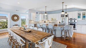 A spacious kitchen with white cabinets, a wooden island, and a dining area with wicker chairs.