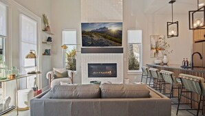 A modern living room with a fireplace, a large painting above it, and a dining area with bar stools.