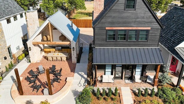 A modern two-story house with a patio area featuring outdoor seating and a barbecue grill.