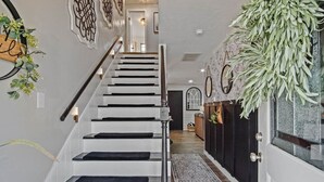 A staircase with black steps and a handrail, leading to a room with a dark door and a plant.