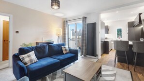 Un salon moderne avec un canapé bleu, une table basse et une vue sur la ville, visible à travers une grande fenêtre.