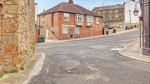 Une vue de rue avec un immeuble en briques de deux étages, un mur de pierre et une voiture garée.