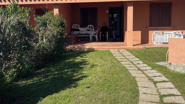 Talo, jossa on tiilikatto, katettu terassi ja pieni nurmikko.