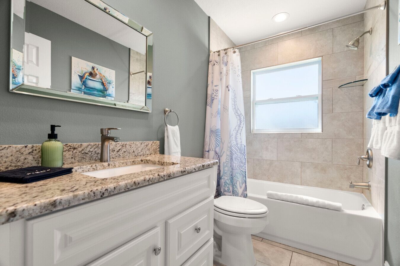 A modern bathroom with a granite countertop, a white toilet, a bathtub, and a shower with a curtain.