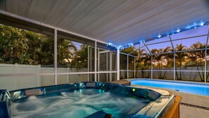 Una vasca idromassaggio con pannello di controllo, una piscina e una zona patio coperta con vista sulle palme.