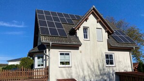 Ett tvåvåningshus med solpaneler på taket, ett garage och en uteplats med utemöbler.
