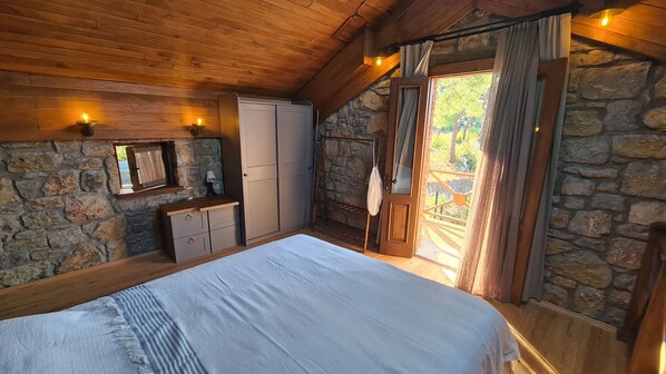 A bedroom with a stone wall, wooden ceiling, a bed, a wardrobe, and a window with curtains.