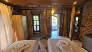 Ein rustikales Zimmer mit zwei Betten, Steinwänden, Holzboden und Blick auf Grünlandschaft.
