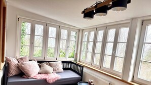 A cozy room with a dark-colored sofa bed, multiple windows, a small round table, and a radiator. - Idyllic house with lots of extras in a beautiful natural setting (Sulzbach-Laufen)