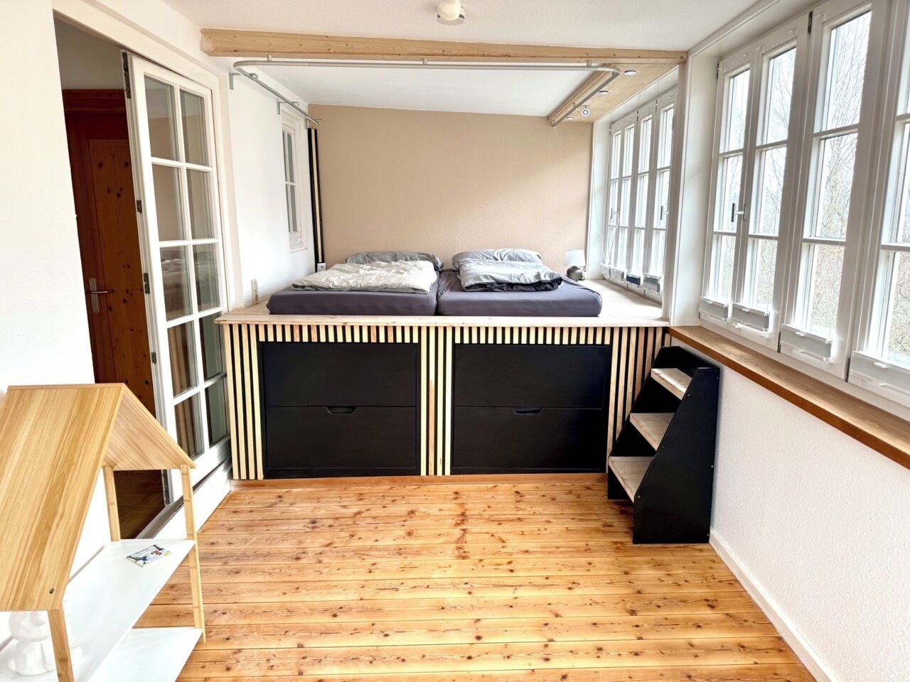 A compact bedroom with a built-in bed, storage drawers, and a windowed alcove.