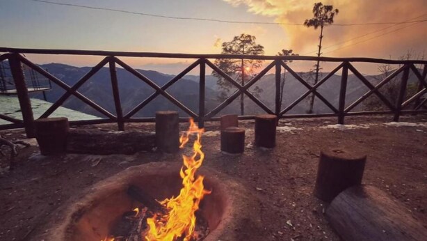 A campfire with a metal railing and a view of mountains in the background.