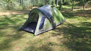 A green and gray tent set up in a grassy area surrounded by trees.