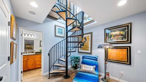 A modern interior with a spiral staircase, wooden cabinets, a blue-striped sofa, and framed artwork on the walls. - Monterey Home Near Aquarium and Cannery Row (Monterey)