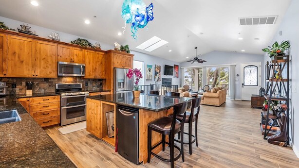 A modern kitchen with wooden cabinets, a central island, and a dining area with bar stools. - Monterey Home Near Aquarium and Cannery Row (Monterey)