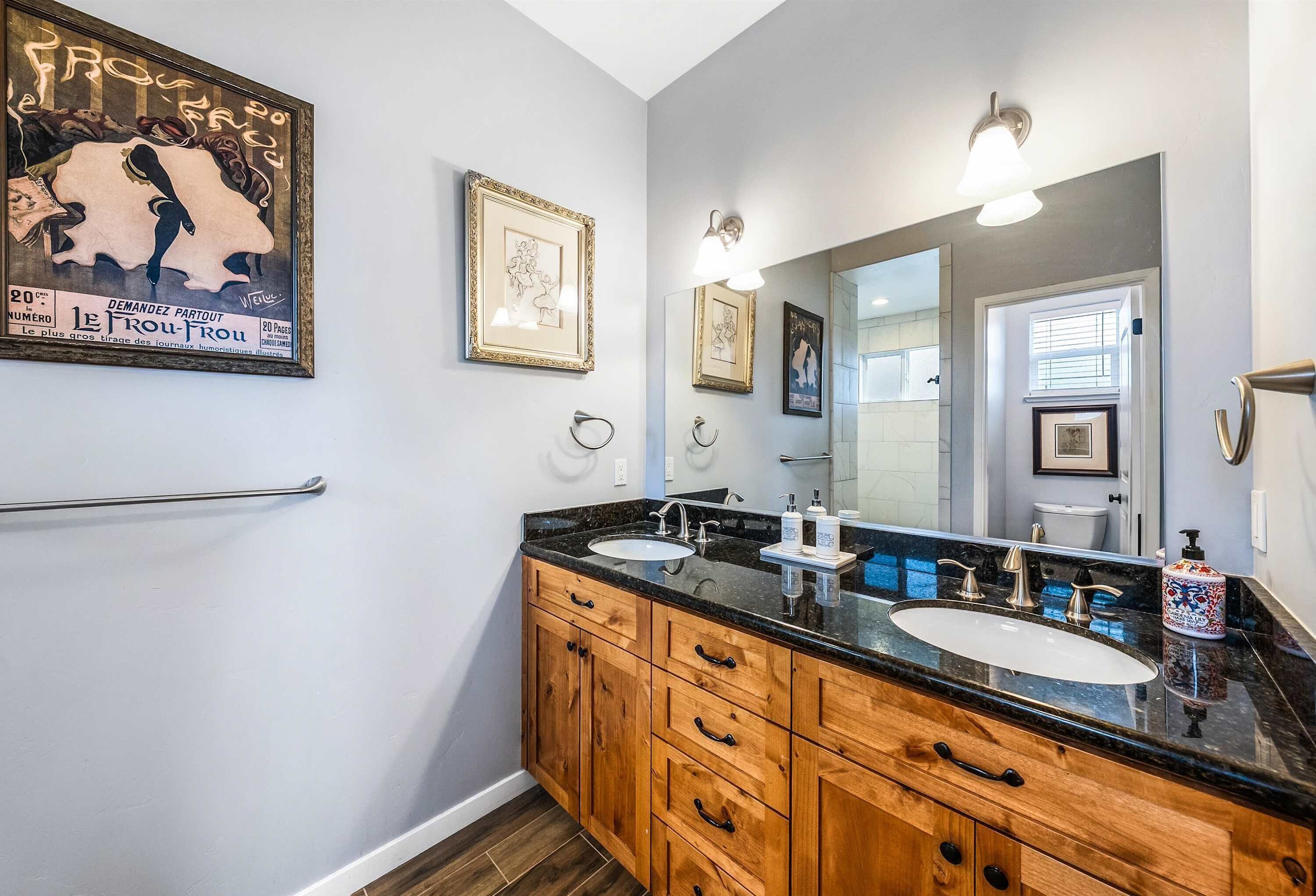 A bathroom with two sinks, wooden cabinets, and framed artwork on the walls.