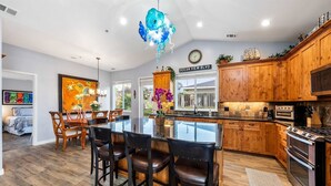 A modern kitchen with wooden cabinets, a central island with bar stools, a large chandelier, and a view of the ocean through the window. - Monterey Home Near Aquarium and Cannery Row (Monterey)
