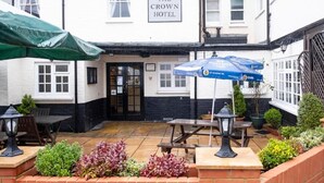 A courtyard with a sign for "The Crown Hotel," outdoor seating with tables and umbrellas, and potted plants. - the crown hotel  (Alton)