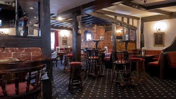 A traditional pub interior with exposed brick walls, wooden beams, and a patterned carpet. Tables and chairs are arranged for dining. - the crown hotel  (Alton)