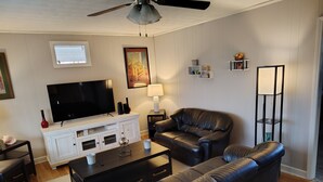 Un salon moderne doté d’un téléviseur à écran plat, de canapés en cuir, d’une table basse et d’un ventilateur de plafond.