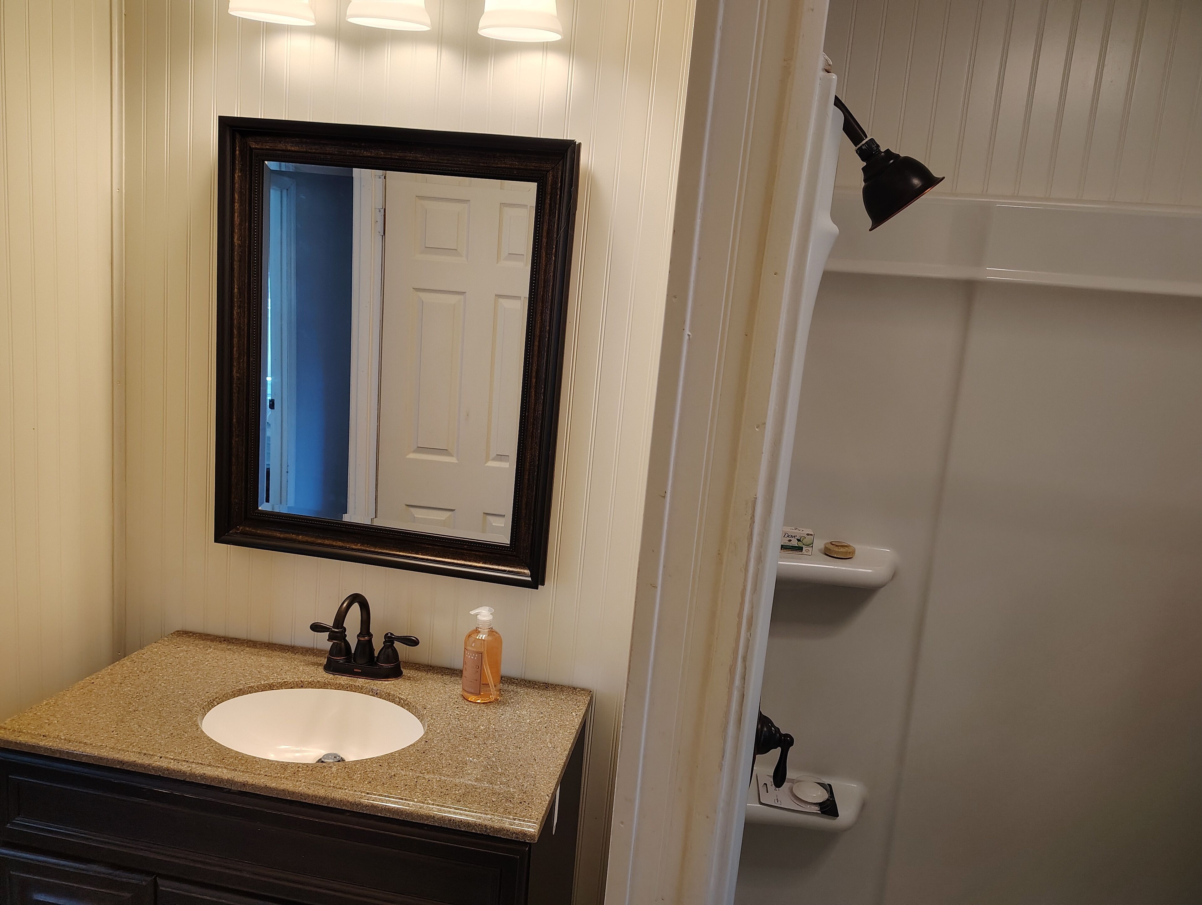 Un baño con lavamanos blanco, encimera de granito oscuro y un espejo encima.