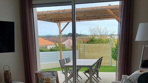 Un salon comprenant un canapé, une table basse et un coin repas avec des chaises et une table. Une porte-fenêtre coulissante donne accès à un patio extérieur équipé d’une table et de chaises.