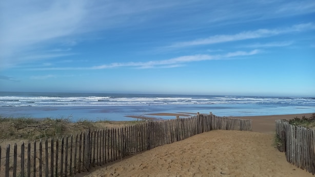 Une plage bordée d’une clôture en bois et un sentier sablonneux menant à l’océan.