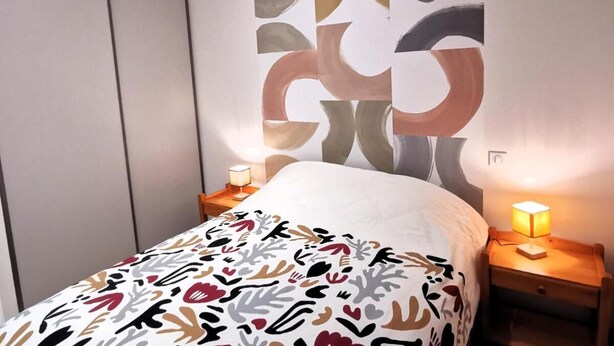 A bedroom with a bed, two bedside tables with lamps, a wardrobe, and abstract wall art. - L'ancrage - house 800m from the beach and shops within walking distance (Brem-sur-Mer)