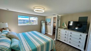 A bedroom with a bed, dresser, television, and a window with a view.