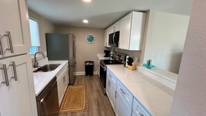 A compact kitchen with white cabinets, a stainless steel refrigerator, a microwave, and a sink.