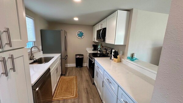 A compact kitchen with white cabinets, a stainless steel refrigerator, a microwave, and a sink.