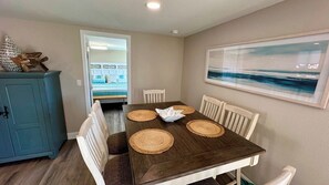 A dining area with a wooden table, white chairs, and a view of the ocean through a window.