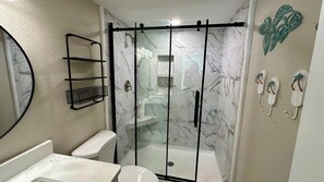 A bathroom with a glass-enclosed shower, a toilet, a sink, and a mirror.