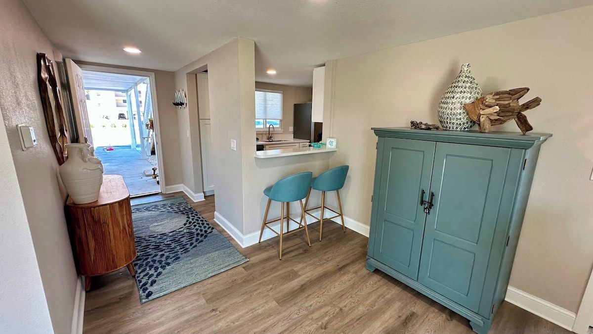 A hallway with a wooden floor, a blue cabinet, and a small seating area with two chairs.