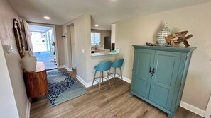 A hallway with a wooden floor, a blue cabinet, and a small seating area with two chairs.