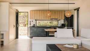 Un salon moderne comprenant un canapé, une table basse et un coin cuisine avec des meubles en bois et des luminaires suspendus.