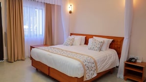 A hotel room with a large bed, a bedside table, and a window with curtains. - Clayton Luxury Suite (Machakos)